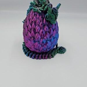 May include: A small, iridescent purple and green dragon egg figurine with detailed scales and a leafy crown.