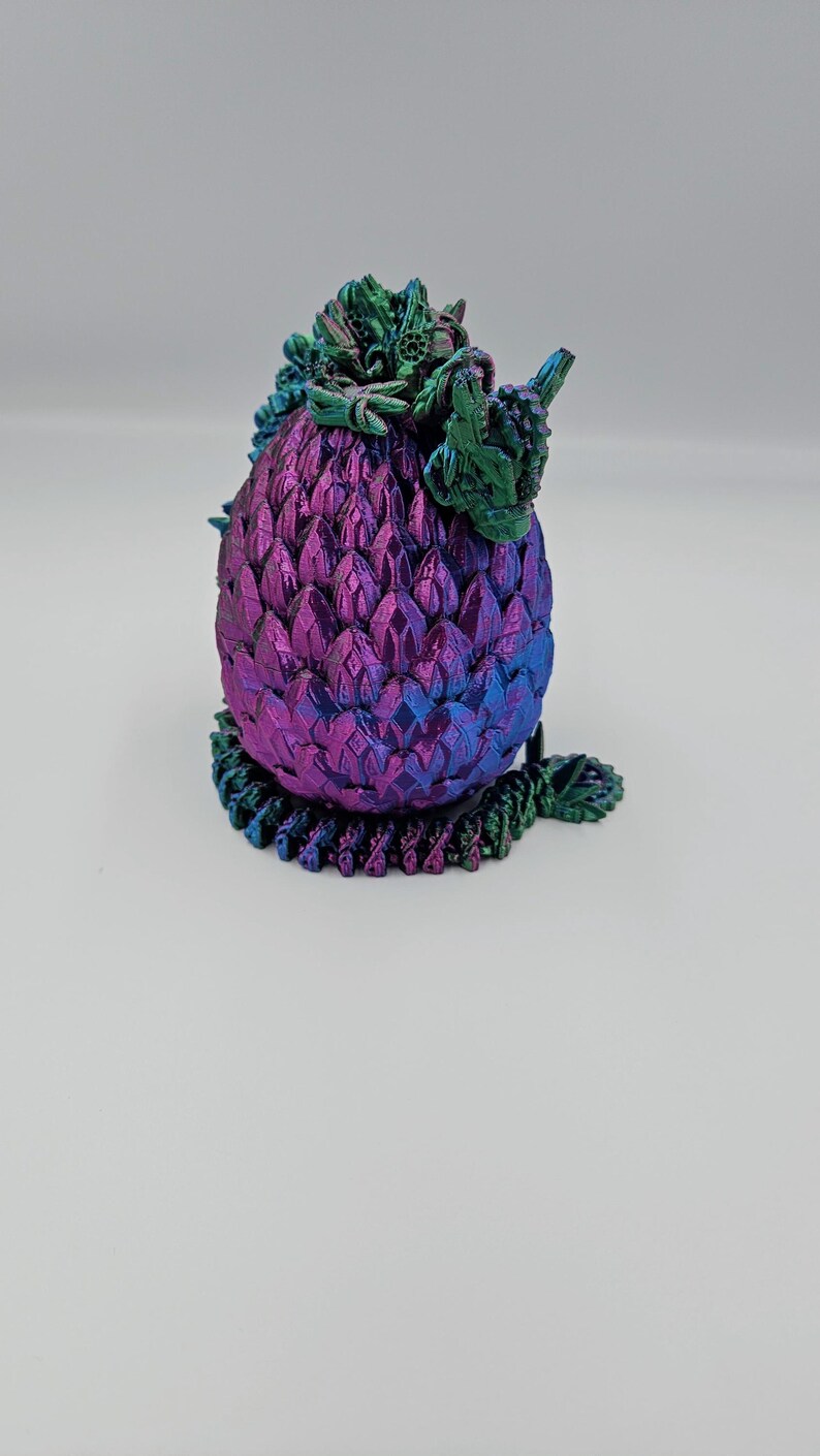 May include: A small, iridescent purple and green dragon egg figurine with detailed scales and a leafy crown.