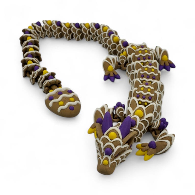 May include: A whimsical, brown dragon sculpture with intricate details. The dragon features a segmented body, adorned with yellow, purple, and white accents. The sculpture has a curved tail and a detailed head, all on a white background.