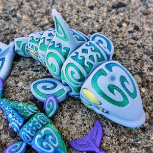 May include: A blue and green 3D printed shark with a swirling pattern. The shark is made of plastic and has a detailed design.