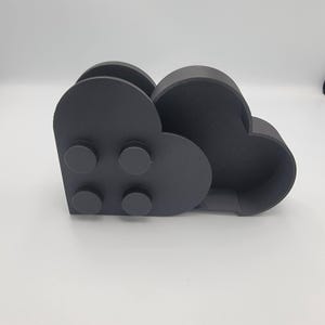 May include: A dark gray, cloud-shaped desk organizer. The organizer has two compartments and four circular details on the front. The item is made of a solid material and sits on a white surface.