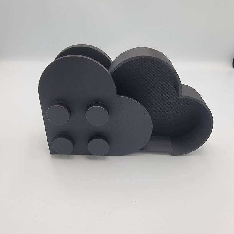 May include: A dark gray, cloud-shaped desk organizer. The organizer has two compartments and four circular details on the front. The item is made of a solid material and sits on a white surface.