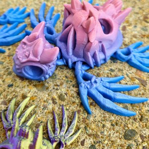 Peut inclure: Un ensemble de sculptures de mains squelettiques imprim&eacute;es en 3D en bleu, rose et jaune avec des accents violets. Les mains sont pos&eacute;es dans diff&eacute;rentes positions, certains doigts &eacute;tant tendus et d'autres recourb&eacute;s.