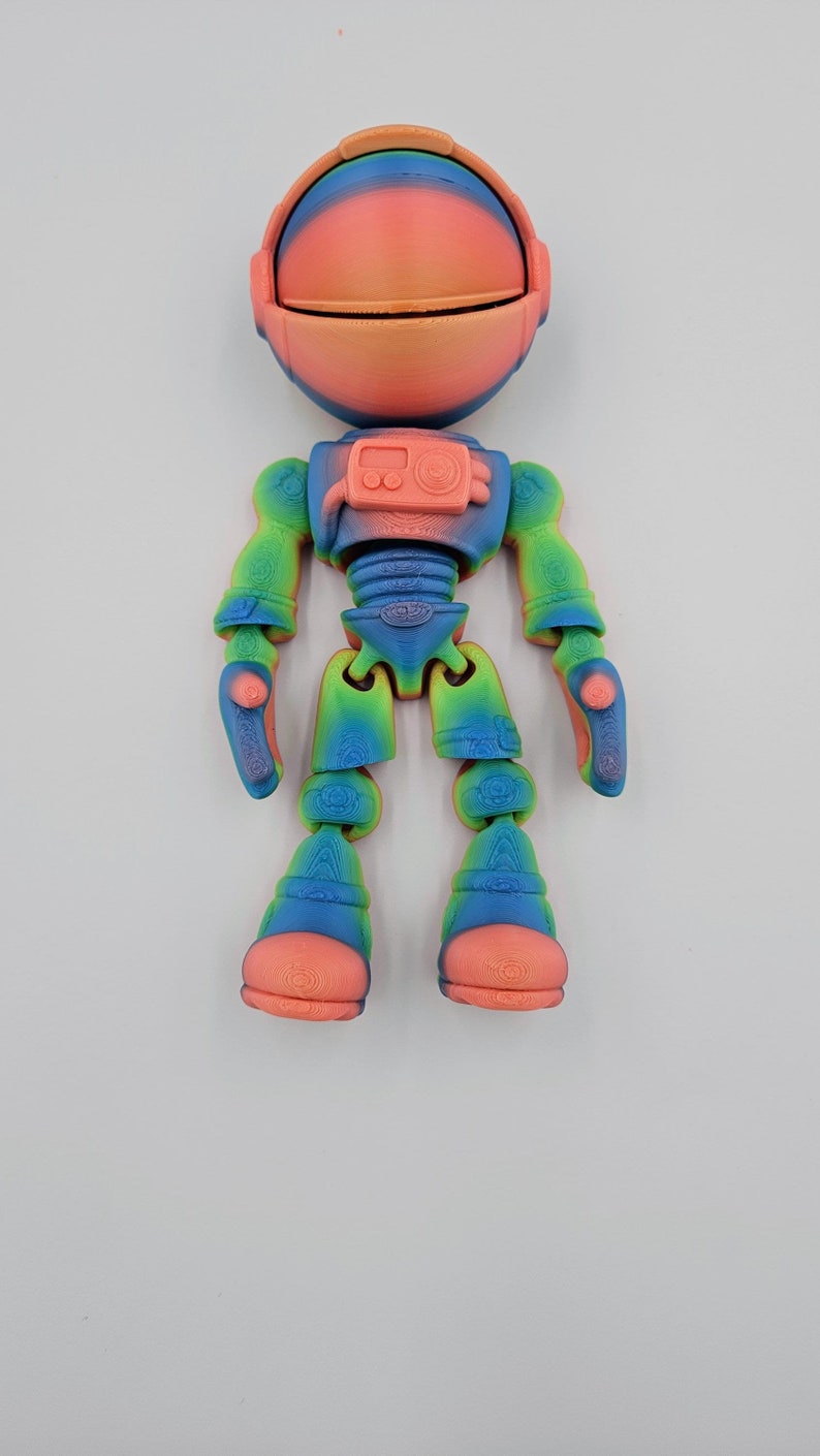 May include: A colorful, articulated astronaut toy with a rainbow gradient and a pink helmet. The toy is made of plastic and has a detailed design.