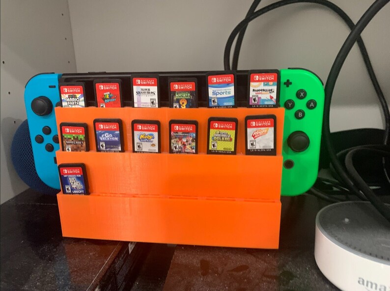 May include: An orange plastic stand holds 18 Nintendo Switch game cartridges. A blue and green Nintendo Switch console is on the right side of the stand.