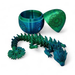 Puede incluir: Un drag&oacute;n impreso en 3D verde y azul con detalles de girasol. El drag&oacute;n est&aacute; hecho de muchas piezas peque&ntilde;as que se pueden conectar entre s&iacute;. El drag&oacute;n est&aacute; sentado sobre un fondo blanco.
