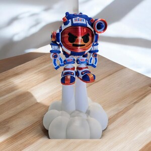 May include: A 3D printed figurine of a red, white and blue robot with an angry face. The robot is standing on a white cloud-shaped base.