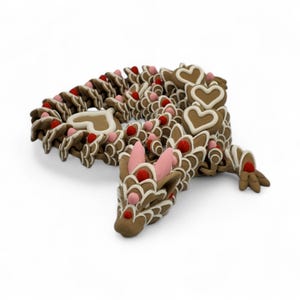 May include: A whimsical, brown dragon sculpture decorated with white icing and red and pink accents. The dragon's body is made of interconnected pieces, with heart-shaped details and a playful design. The sculpture is set against a white background.