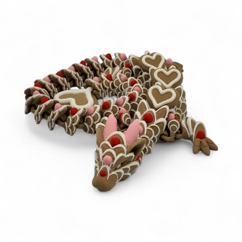 May include: A whimsical, brown dragon sculpture decorated with white icing and red and pink accents. The dragon's body is made of interconnected pieces, with heart-shaped details and a playful design. The sculpture is set against a white background.