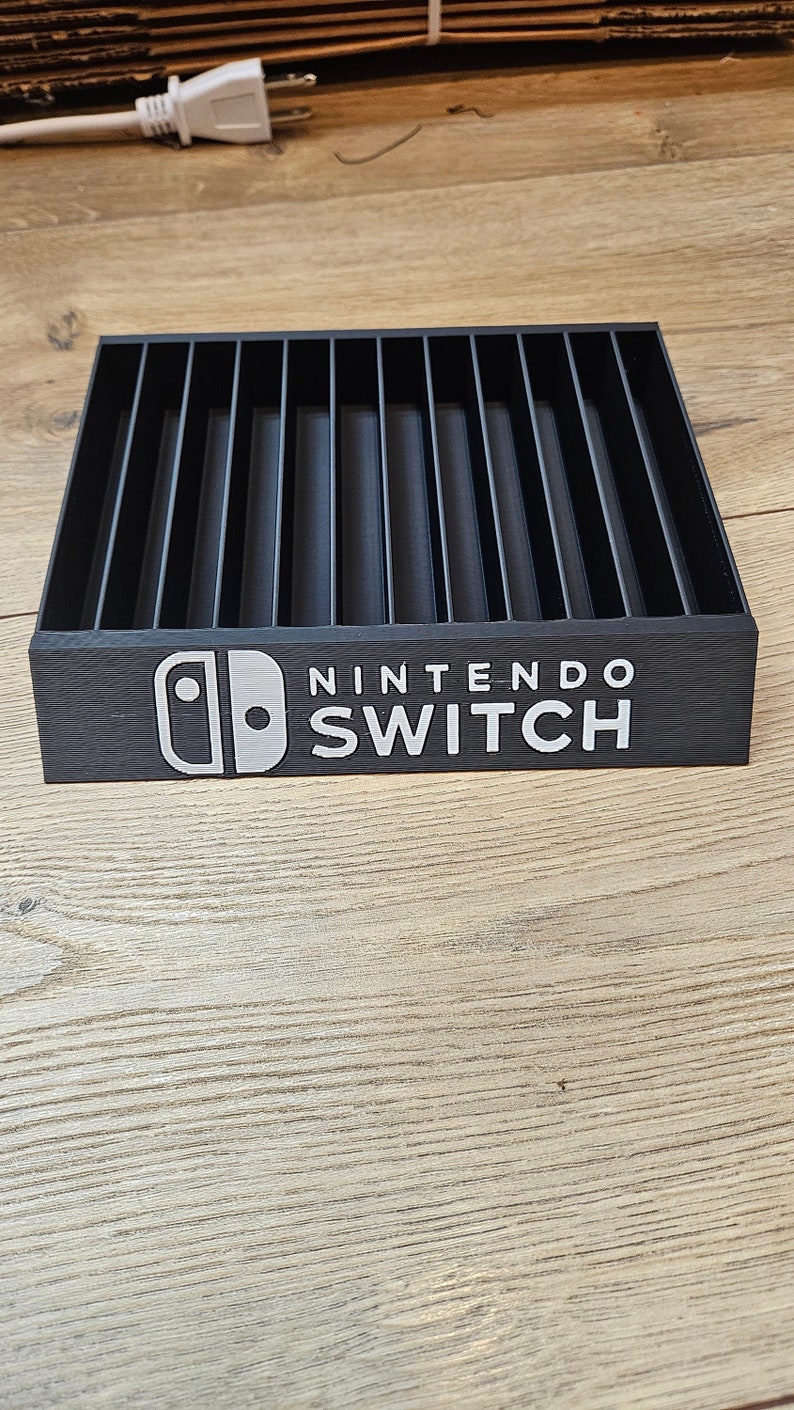 May include: Black plastic Nintendo Switch game cartridge storage case with 16 slots. The case has the Nintendo Switch logo and the words "Nintendo Switch" printed on the front.