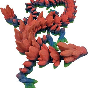 K&ouml;nnte beinhalten: Eine 3D-gedruckte Drachenfigur mit einem rot-blau-gr&uuml;nen Farbschema. Der Drache besteht aus vielen kleinen, spitzen Kristallen.