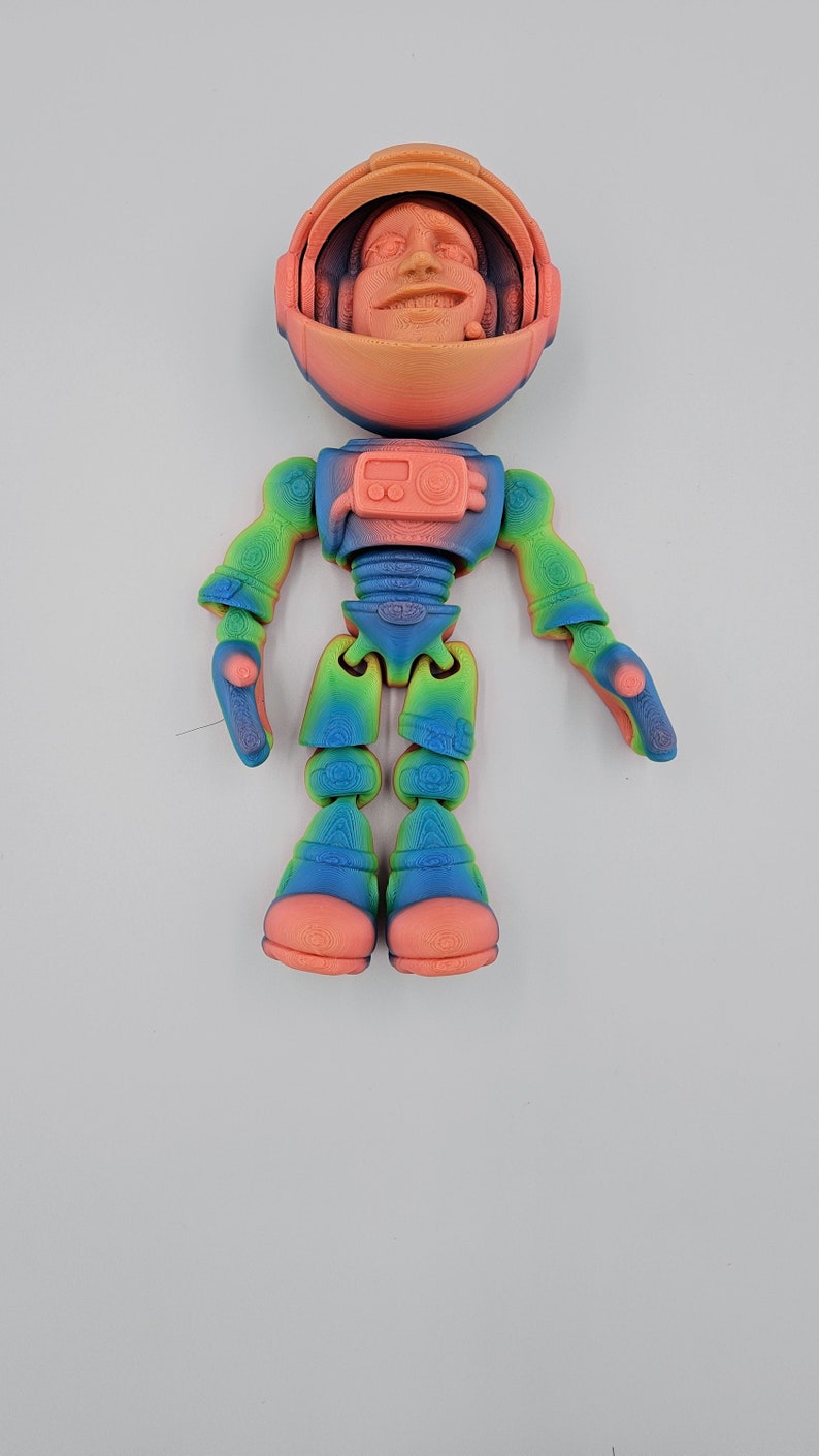 May include: A 3D printed astronaut figurine with a rainbow gradient color scheme. The astronaut has a human face and is wearing a helmet. The figurine is articulated and has movable arms and legs.