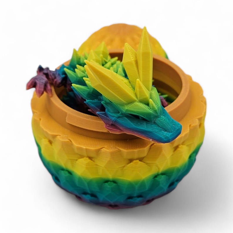 May include: A 3D-printed, multi-colored dragon figurine emerging from a round container. The dragon's head and the container are in shades of yellow, green, blue, and purple. The container has a textured, geometric design.