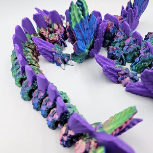 May include: A 3D printed dragon figurine with iridescent purple, green, and blue scales. The dragon is curled up in a defensive posture with its wings spread out.