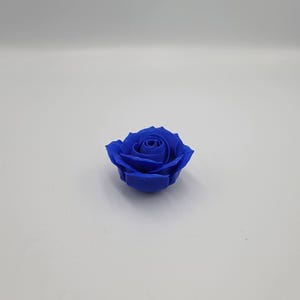 May include: A single, vibrant blue rose. The flower is in full bloom, with tightly packed petals forming a spiral center. The rose is set against a plain white background, highlighting its color and form. This could be a decorative item or a craft supply.