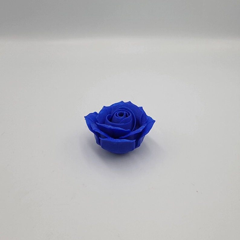 May include: A single, vibrant blue rose. The flower is in full bloom, with tightly packed petals forming a spiral center. The rose is set against a plain white background, highlighting its color and form. This could be a decorative item or a craft supply.