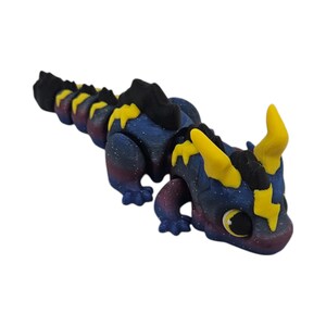 K&ouml;nnte beinhalten: Eine bewegliche Drachenfigur. Der Drache hat einen dunkelblauen K&ouml;rper mit einem galaxieartigen Muster, gelben blitzf&ouml;rmigen Details und H&ouml;rnern. Der Bauch des Drachen geht in ein tiefes Rot &uuml;ber.