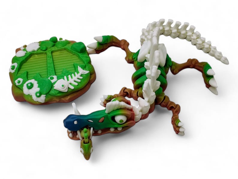 May include: A green and white skeletal dragon figurine with a green and brown base. The dragon has a long tail and a large head with a toothy grin. The base has a green and brown design with white flowers and fish bones.
