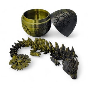 Puede incluir: Una figurita de drag&oacute;n segmentada impresa en 3D, negra y dorada. El drag&oacute;n est&aacute; enroscado y tiene una superficie texturizada detallada. El drag&oacute;n est&aacute; en un recipiente redondo y dorado cerrado con un dise&ntilde;o de girasol.