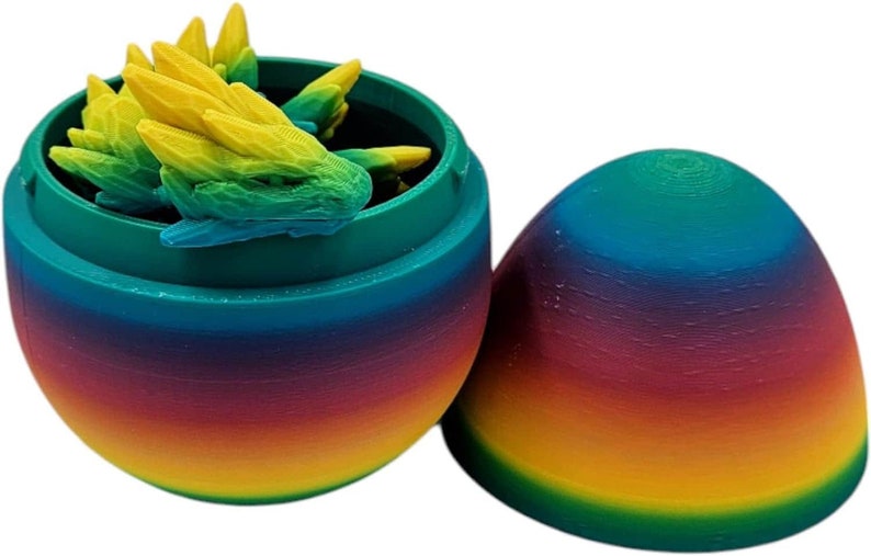 May include: A rainbow-coloured plastic egg with a green lid, open to reveal a set of small, green and yellow dinosaur figurines inside.