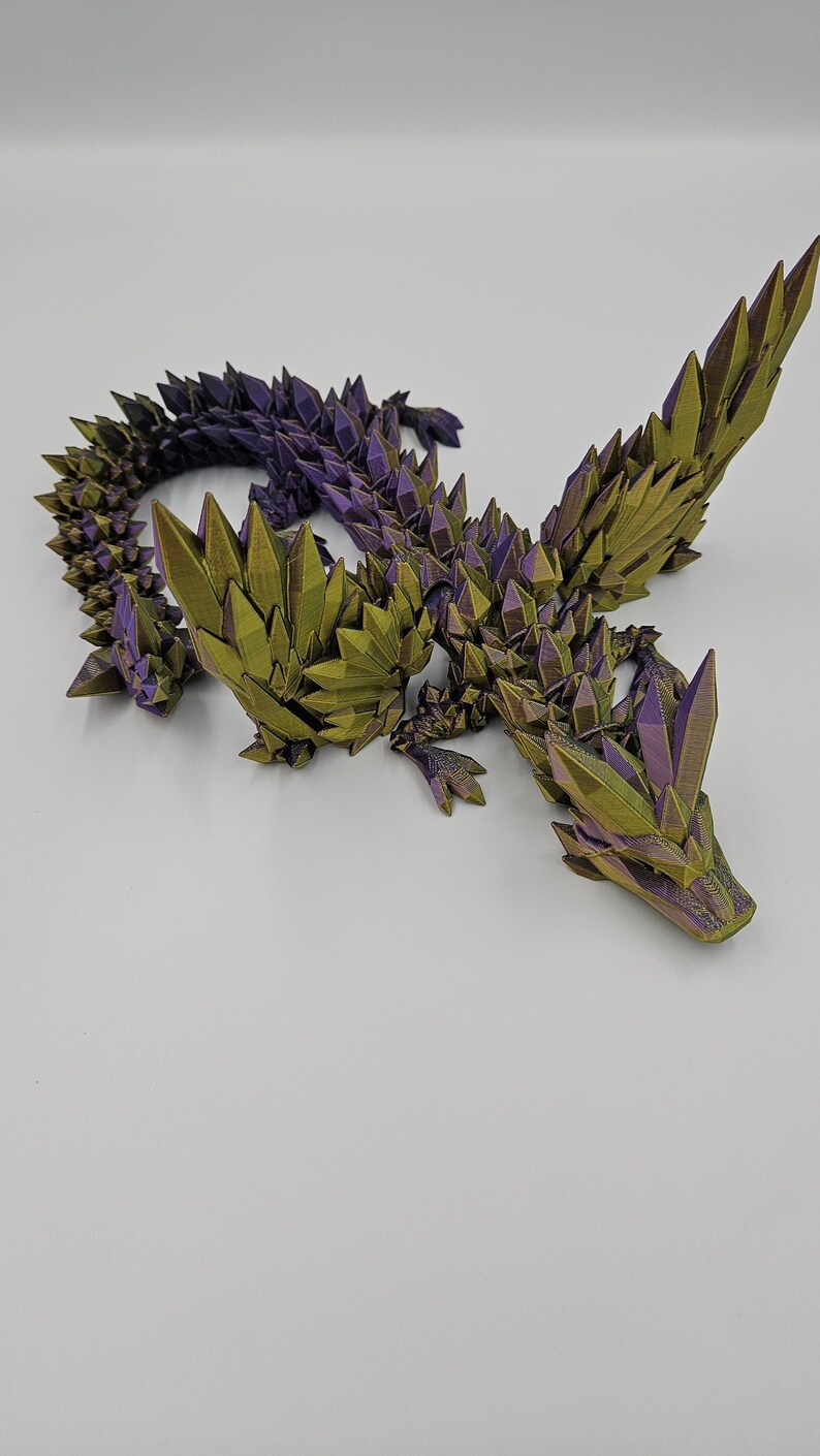 May include: A 3D printed dragon figurine with a green and purple iridescent finish. The dragon is posed in a crawling position with its wings spread out.