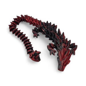 May include: A 3D printed dragon figurine with a black and red color scheme. The dragon is curled up with its tail wrapped around its body.