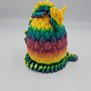 May include: A 3D printed dragon egg with a rainbow color scheme. The egg is made of plastic and has a textured surface. The dragon egg is a decorative item.