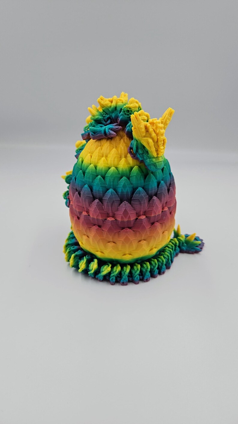 May include: A 3D printed dragon egg with a rainbow color scheme. The egg is made of plastic and has a textured surface. The dragon egg is a decorative item.