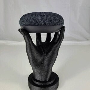 Op de afbeelding: Een zwarte 3D-geprinte hand die een zwarte slimme speaker vasthoudt.