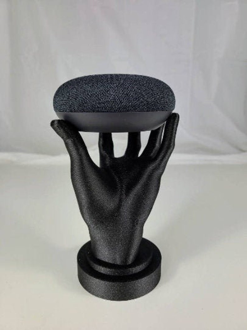 Op de afbeelding: Een zwarte 3D-geprinte hand die een zwarte slimme speaker vasthoudt.