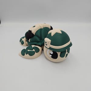 Pode incluir: Figura de tartaruga artesanal com carapa&ccedil;a e cabe&ccedil;a verde escuro, e detalhes em branco sujo. A tartaruga tem olhos grandes e um design divertido. Um objeto decorativo charmoso.