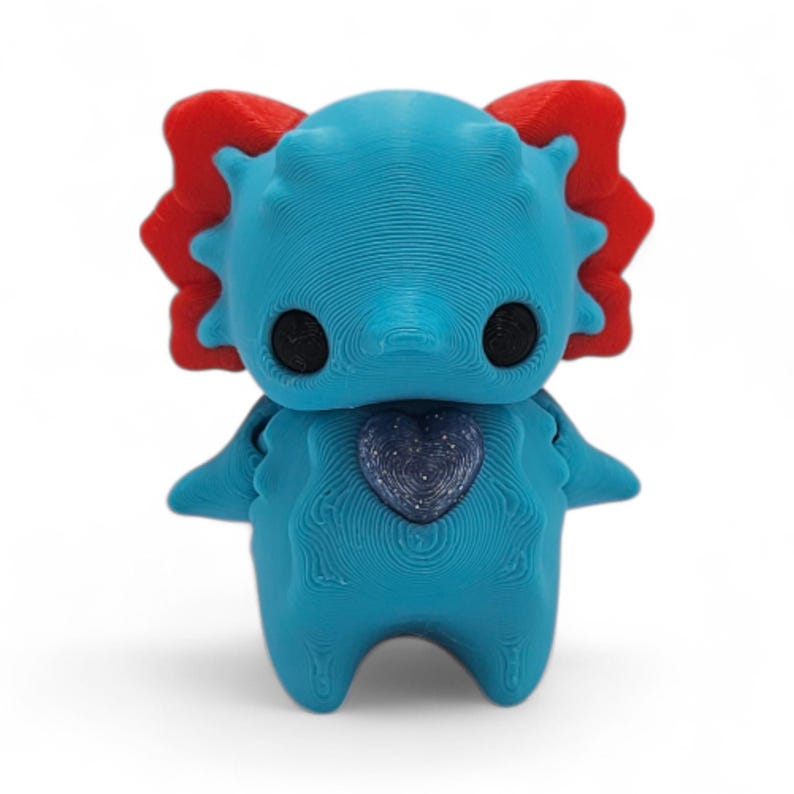 May include: A 3D-printed figurine of a cartoonish creature in shades of blue and red. The figure has large black eyes, a heart-shaped design on its chest, and a textured surface. The creature has a whimsical design.