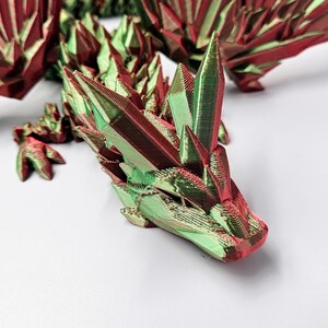 May include: A 3D printed dragon figurine with a green and red iridescent finish. The dragon is posed with its head raised and its wings spread out.