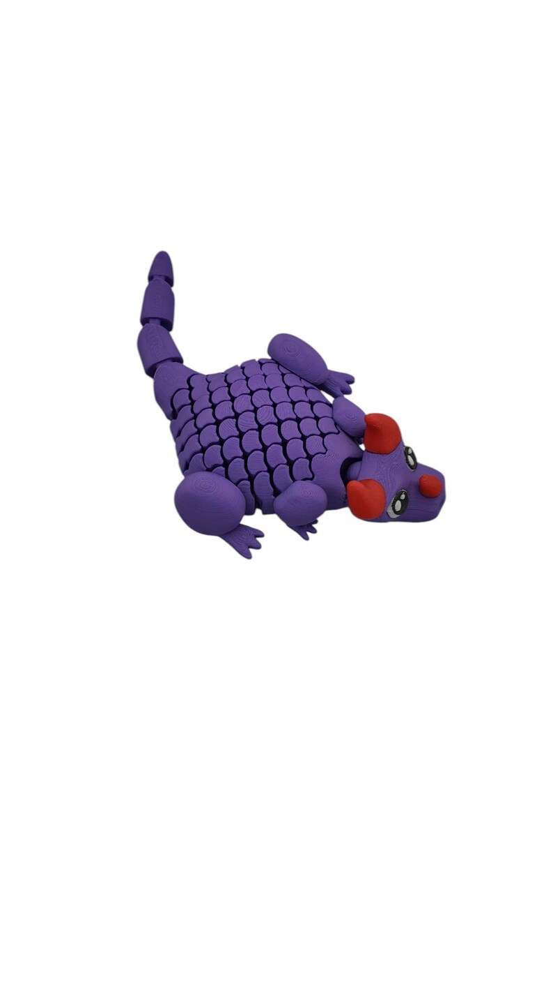 Puede incluir: Un juguete de drag&oacute;n articulado morado con un cuerpo y cola segmentados. El drag&oacute;n tiene detalles rojos en la cabeza y est&aacute; posado sobre un fondo blanco. El juguete est&aacute; dise&ntilde;ado con un patr&oacute;n de escamas.