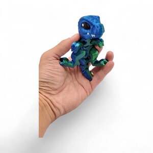 May include: A blue and green 3D puzzle of a dinosaur. The dinosaur is standing on its hind legs with its mouth open and its eyes closed. The puzzle is made of plastic and is about 5 inches tall.