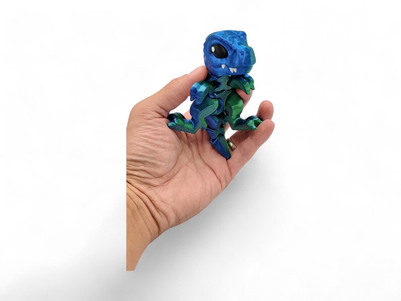 May include: A blue and green 3D puzzle of a dinosaur. The dinosaur is standing on its hind legs with its mouth open and its eyes closed. The puzzle is made of plastic and is about 5 inches tall.