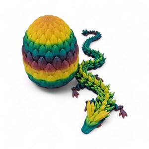 May include: A 3D-printed dragon and egg set. The egg is a vibrant gradient of yellow, green, blue, and purple. The dragon has a matching color scheme with a spiky design, and is posed next to the egg.