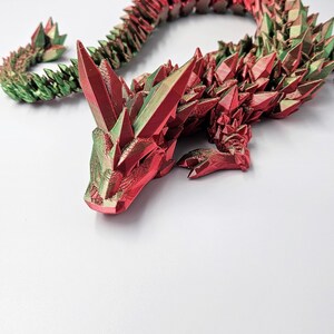 May include: A 3D printed dragon figurine with a red and green iridescent finish. The dragon is curled up in a sleeping position with its head resting on its front paws.