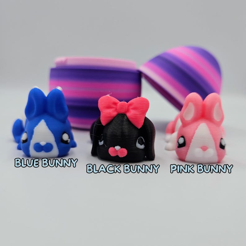K&ouml;nnte beinhalten: Drei kleine Hasenfiguren, eine blaue, eine schwarze mit einer rosa Schleife und eine rosa. Die Hasen schauen alle nach vorne und haben die Augen geschlossen.