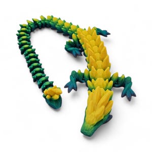 May include: A 3D printed lizard figurine with a yellow and green gradient color scheme. The lizard has a long, segmented tail and a spiky, crystalline back.