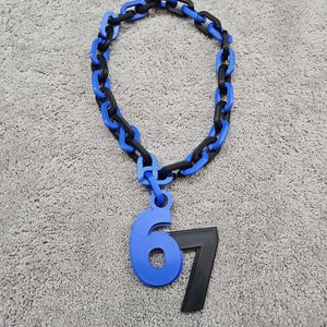 May include: A blue and black chain necklace with a pendant featuring the numbers 6 and 7. The number 6 is blue, and the number 7 is black. The chain links alternate between blue and black.