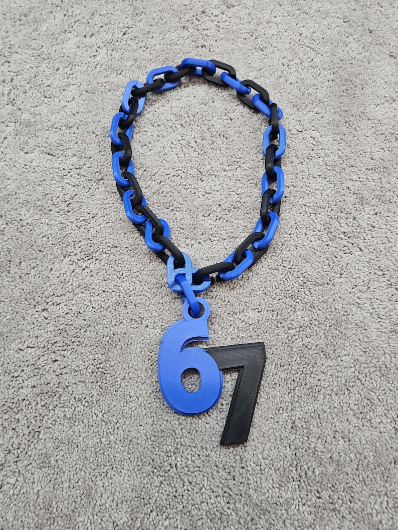 May include: A blue and black chain necklace with a pendant featuring the numbers 6 and 7. The number 6 is blue, and the number 7 is black. The chain links alternate between blue and black.