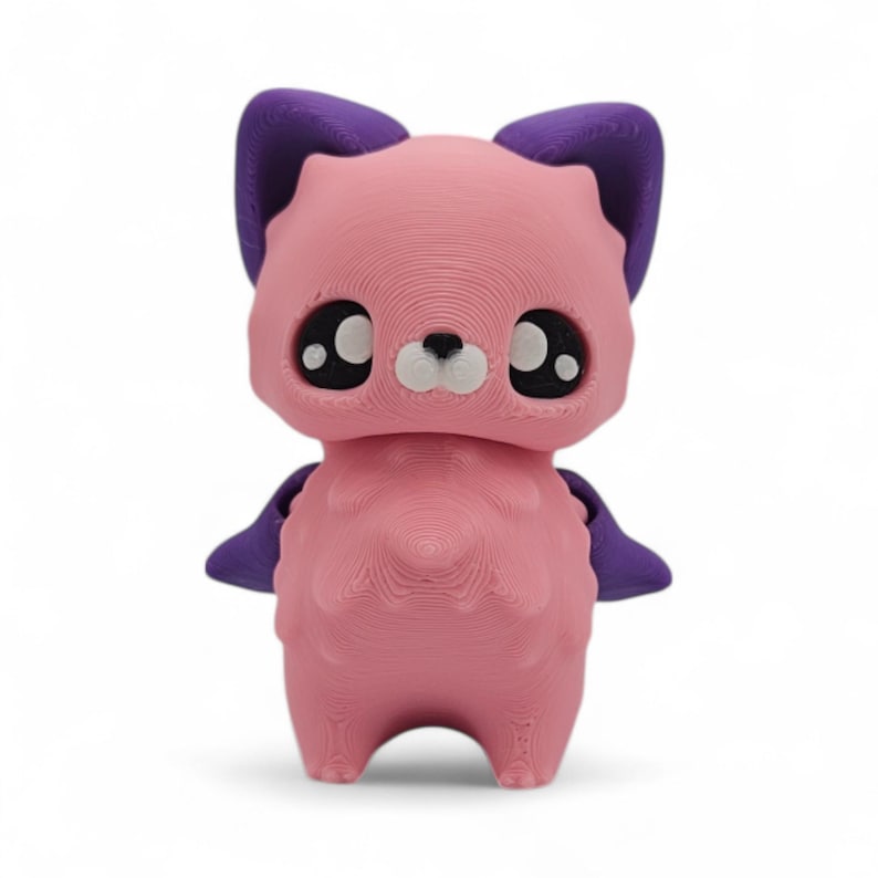 May include: A pink 3D-printed figurine of a stylized animal with large eyes, purple ears, and small purple wings. The figurine has a textured surface and a cute, friendly appearance, perfect for a child's room or as a decorative item.