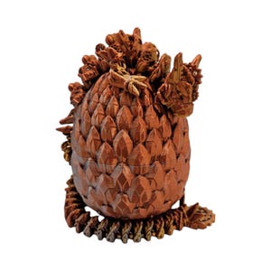 May include: A 3D printed dragon egg with a textured, scaly surface. The egg is a reddish-brown color and has a detailed, intricate design.