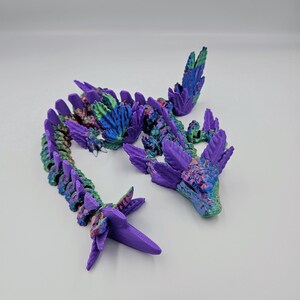 May include: A 3D printed dragon figurine with a purple and green iridescent finish. The dragon is segmented and has wings.