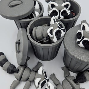 May include: Gray 3D-printed raccoon figurines with articulated limbs and black and white markings. The raccoons are in and around small gray trash cans, some with lids. The image is a playful depiction of a common theme.