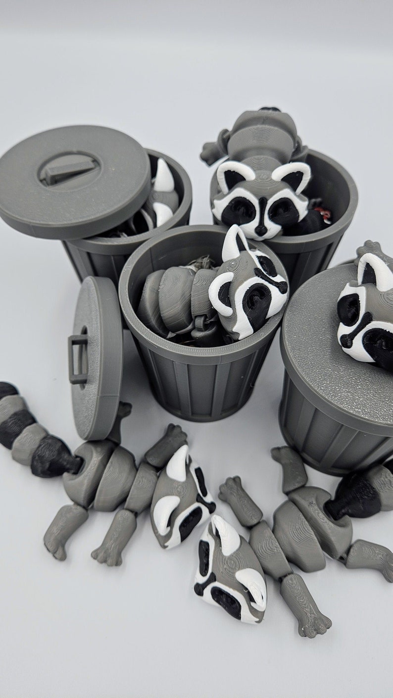 May include: Gray 3D-printed raccoon figurines with articulated limbs and black and white markings. The raccoons are in and around small gray trash cans, some with lids. The image is a playful depiction of a common theme.