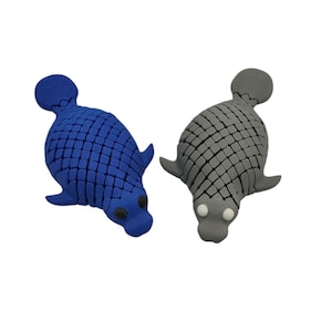 Puede incluir: Dos objetos con forma de foca. Uno es azul, el otro gris. Ambos tienen un patr&oacute;n texturizado en forma de escamas en sus cuerpos, con peque&ntilde;as aletas y una cabeza redondeada. La foca azul tiene ojos negros, la foca gris tiene ojos blancos.