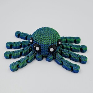 Op de afbeelding: Een blauwe en groene 3D-geprinte octopus met grote witte ogen. De octopus heeft acht gesegmenteerde armen.