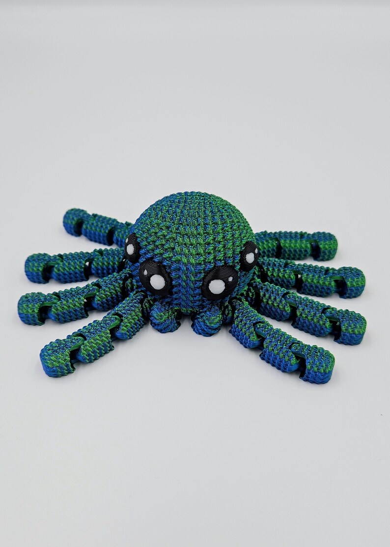 Op de afbeelding: Een blauwe en groene 3D-geprinte octopus met grote witte ogen. De octopus heeft acht gesegmenteerde armen.